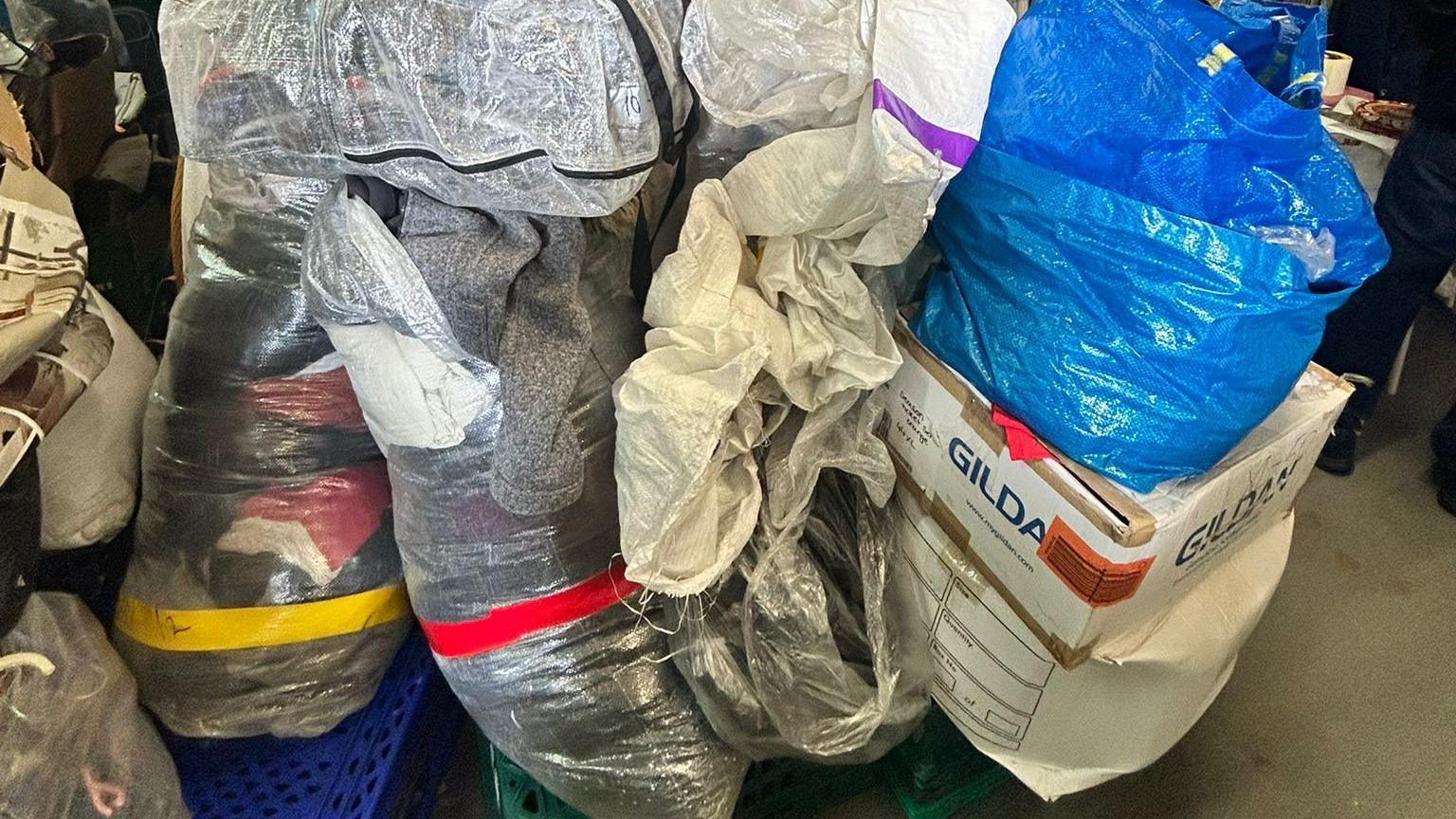 Bags and boxes of clothes lying in a warehouse.