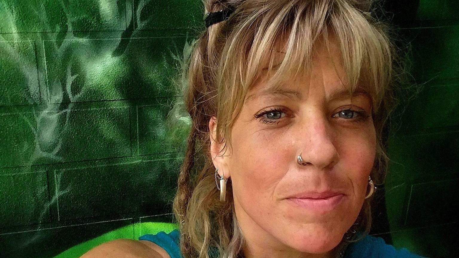 Anna Wheelhouse with blonde bangs standing in front of her green mural