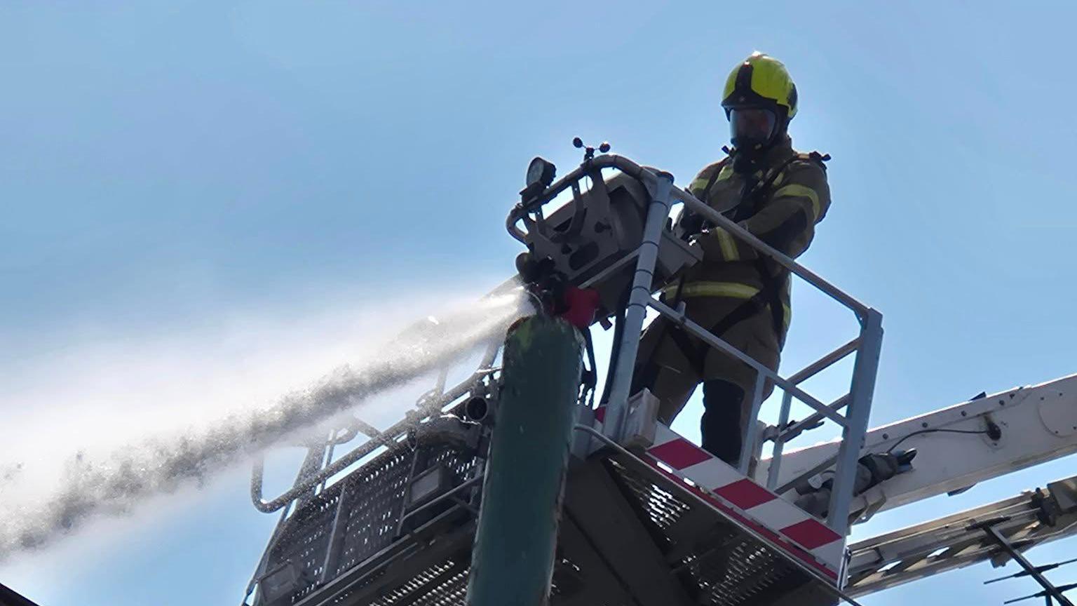 Water being hosed from an aerial platform by a firefighter in kit