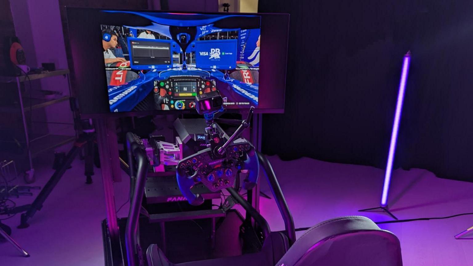 A simulator racing rig with a steering wheel controller in front of a big curved screen. Beneath that are two pedals and a reclined seat in black leather