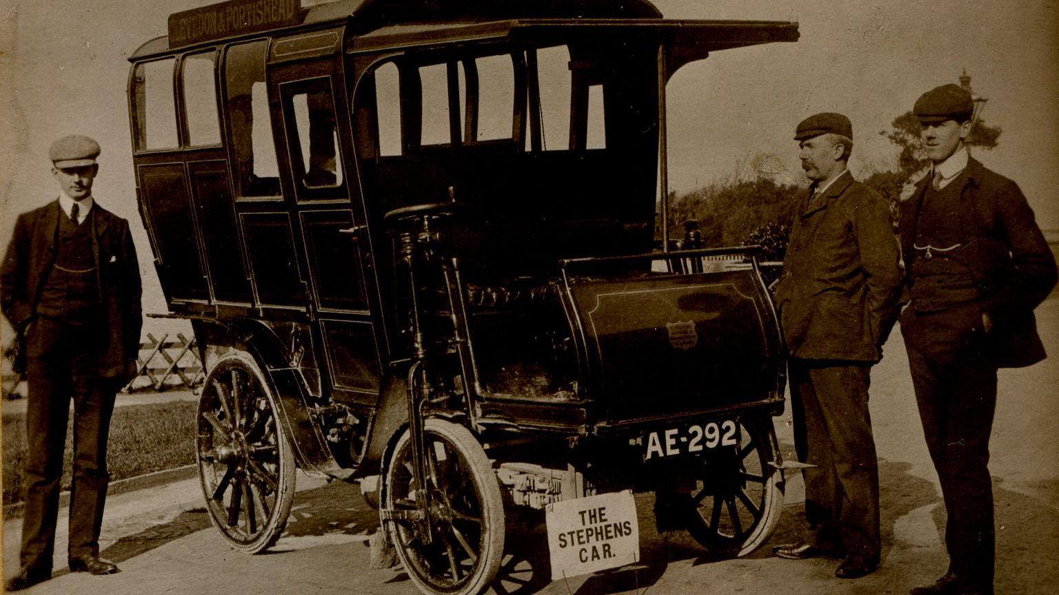 A nine-seater bus with three men in Victorian outfits standing by it