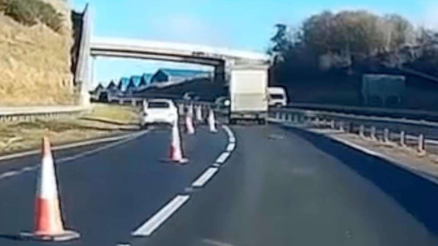 Dashcam footage of a white car going into a coned off part of the dual carriageway to undertake a lorry