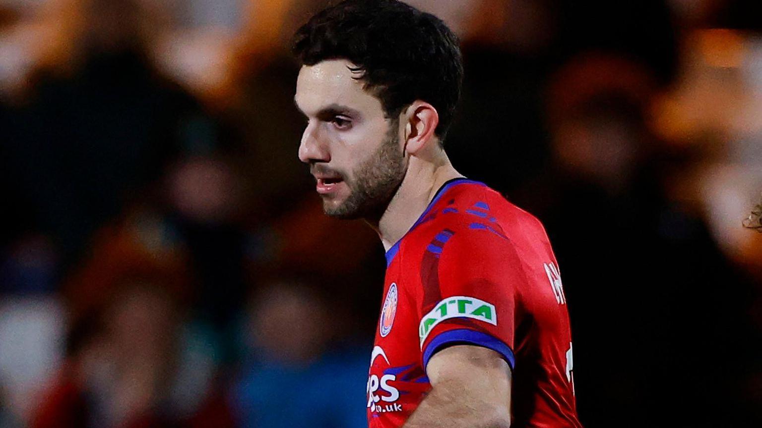 Footballer Hady Ghandour playing football for Aldershot Town while looking to his right and wearing a red shirt with blue trim