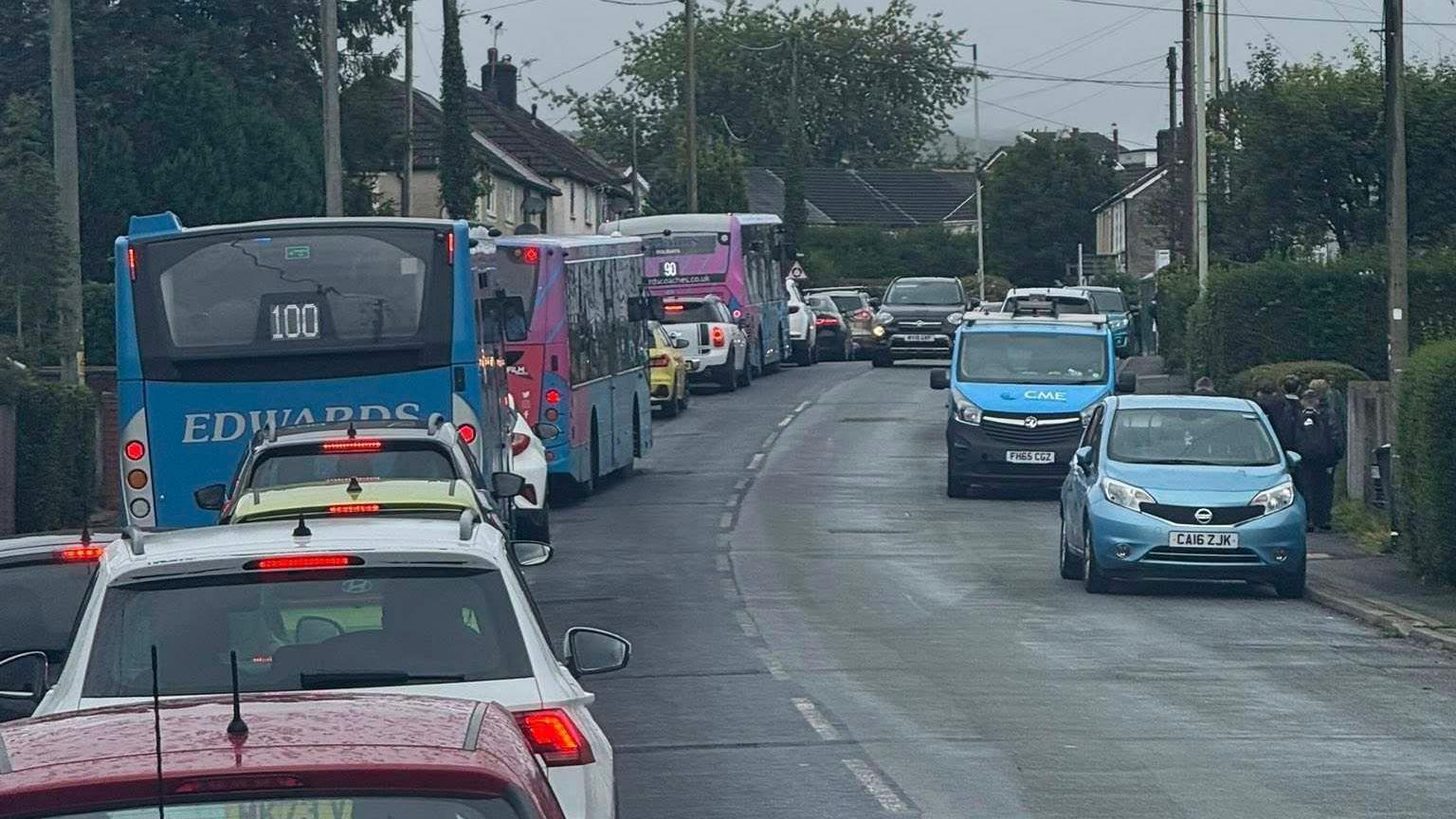 A traffic jam with several cars sitting behind coaches that have been deployed to take pupils to school.