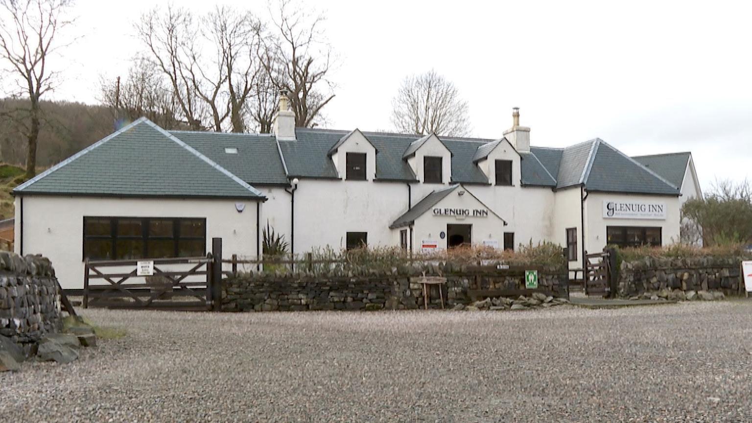 The exterior of the white-walled Glenuig Inn. It is a two storey building and has two signs that read: "Glenuig Inn".