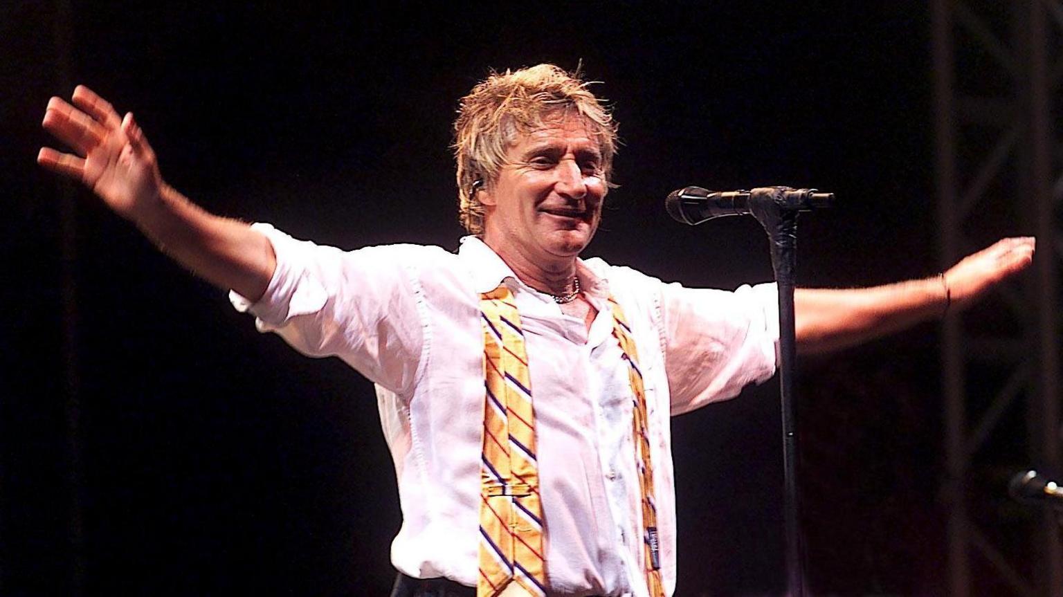 Rod Stewart stretches out his arms to greet the Glastonbury crowd during a performance in 2002