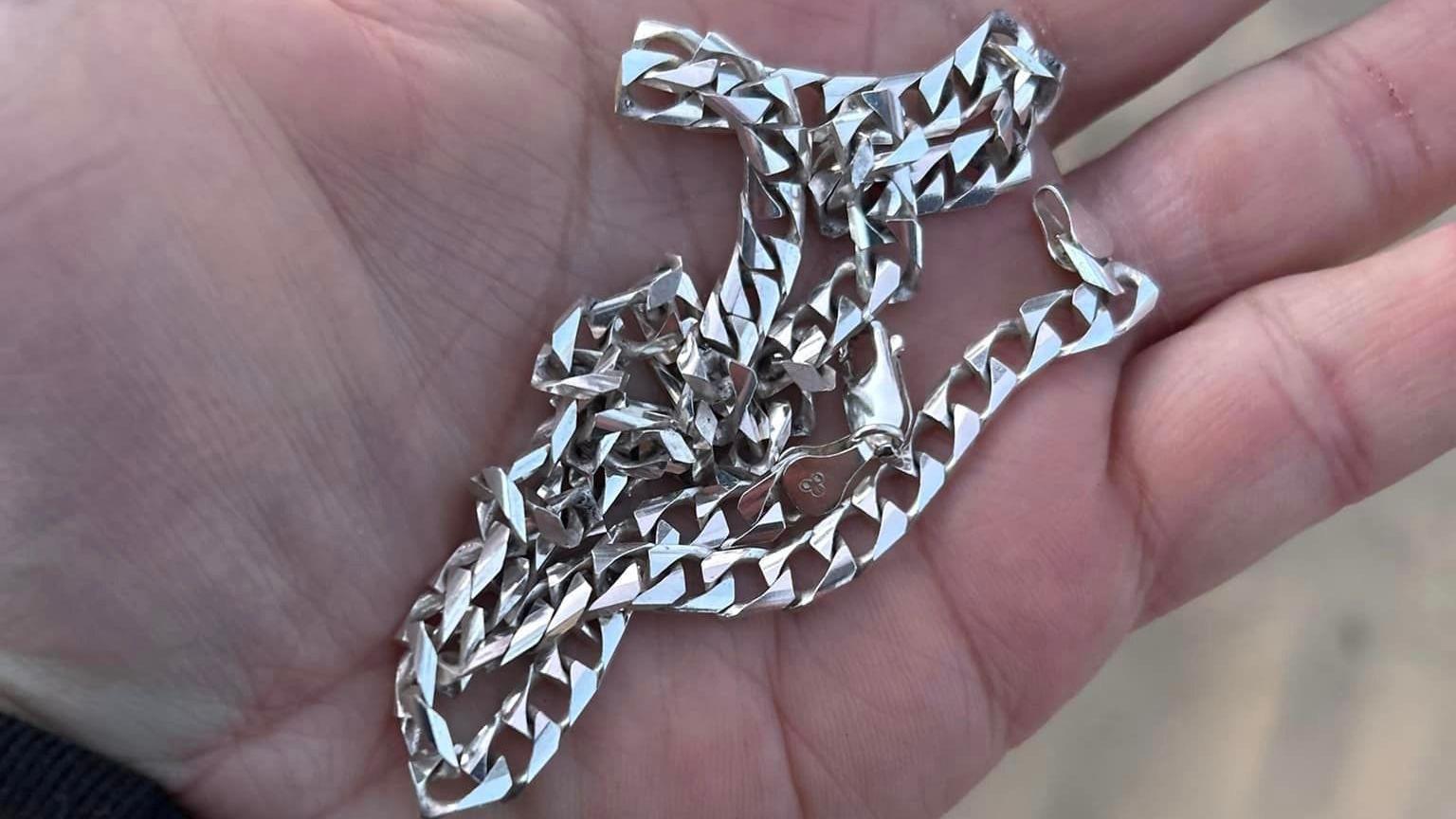 A close-up of an outstretched palm of a hand holding a chunky silver chain