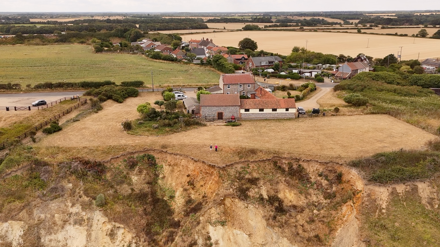 A photograph of an area of Trimingham in north Norfolk. The village is partly built on sandy cliffs on the coastline. The picture is an aerial and has been taken with a drone. It is not looking out to sea but captures how close housing is to the cliff top edge. 