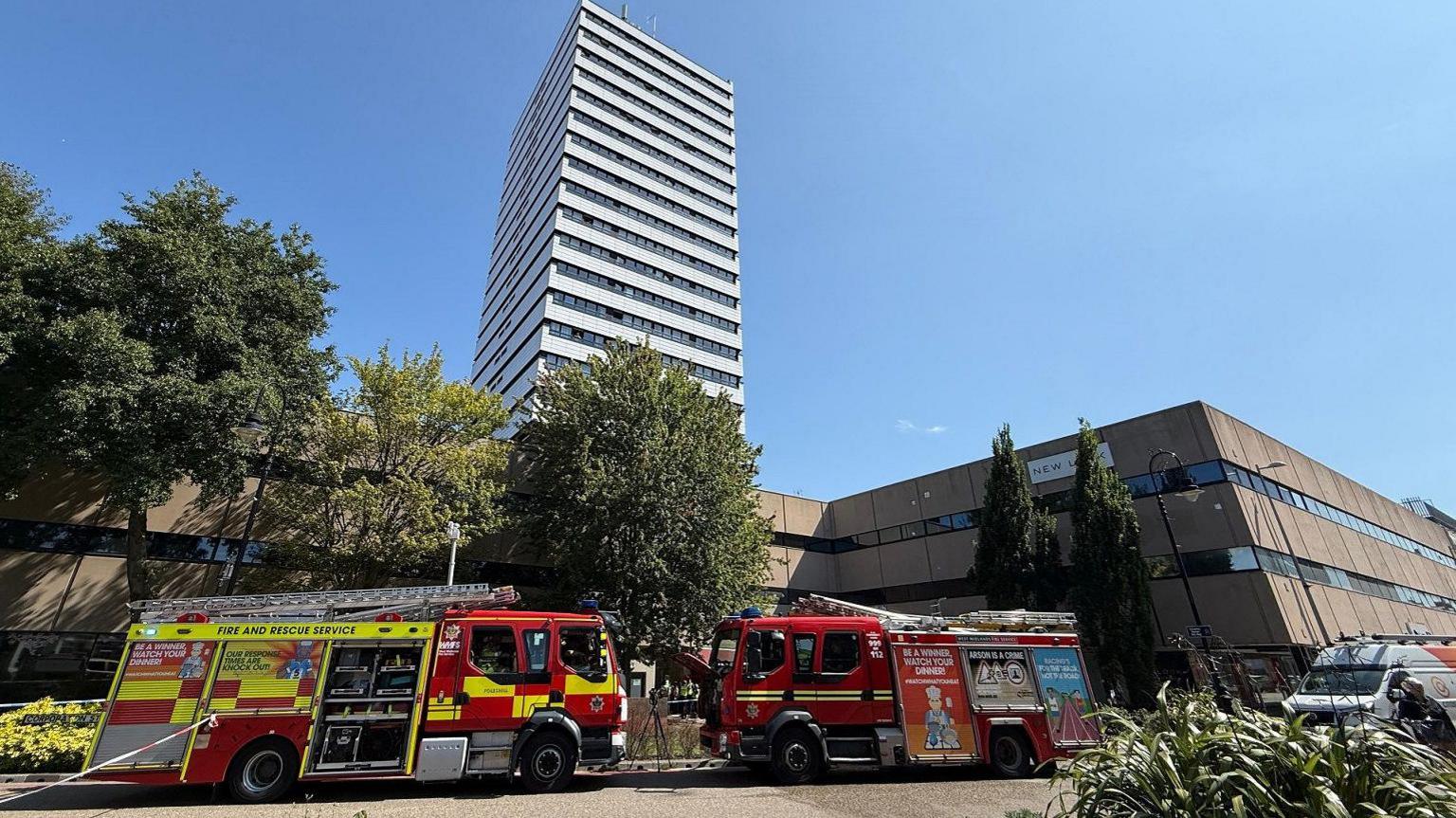 A number of fire trucks and cars parked outside the front of a tower block