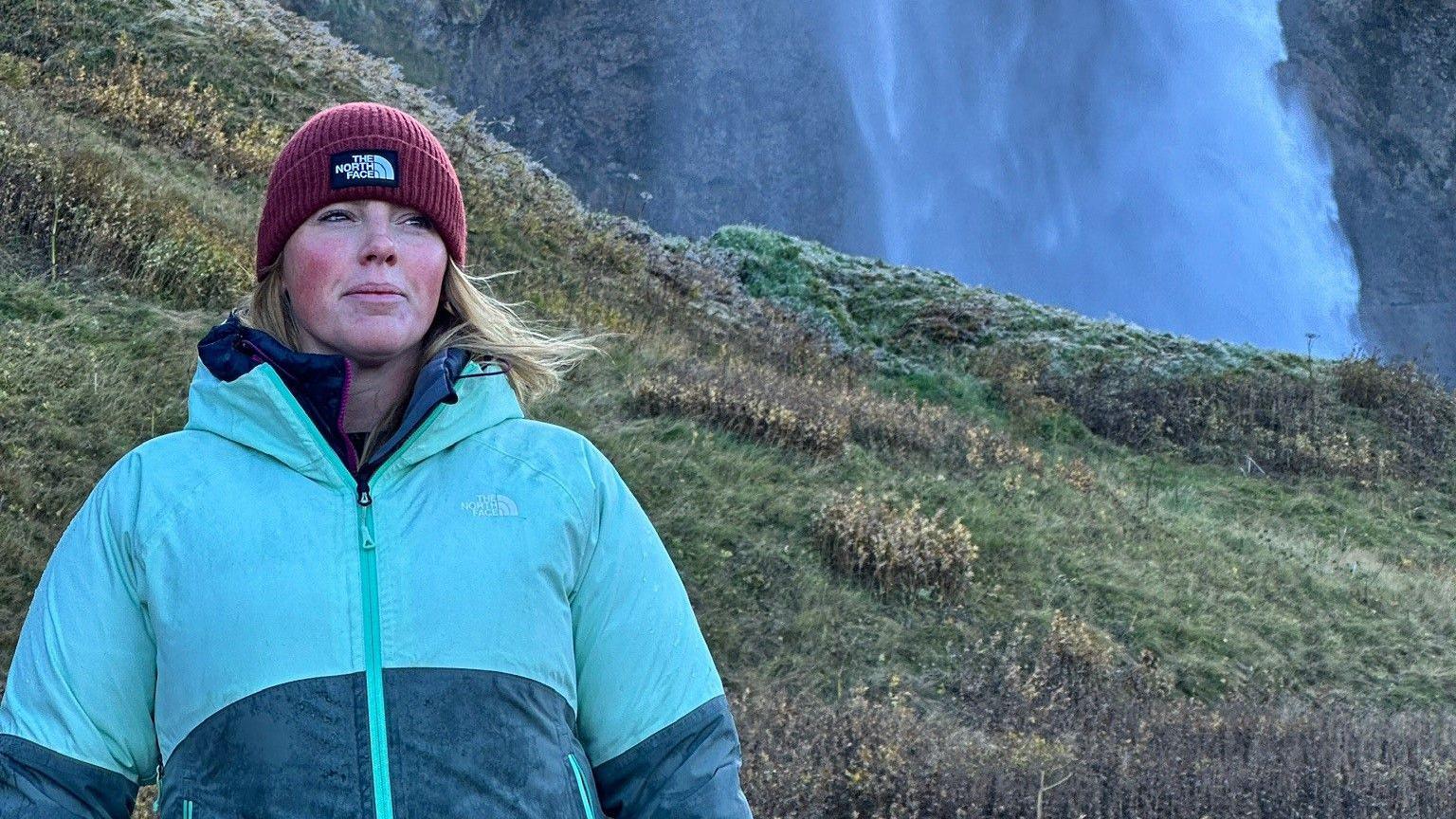 Sarah Meenan stands in the countryside in north Wales. She is wearing hiking gear and a woolly hat and looking away from the camera, inspired by the landscape.