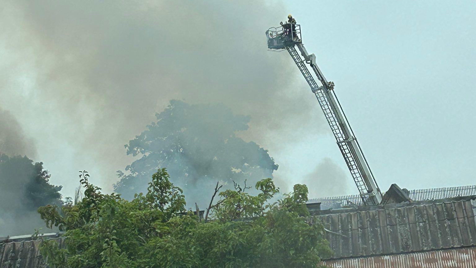 An aerial platform with a fire fighter standing on top, stretched high above the roof of a burning derelict building.