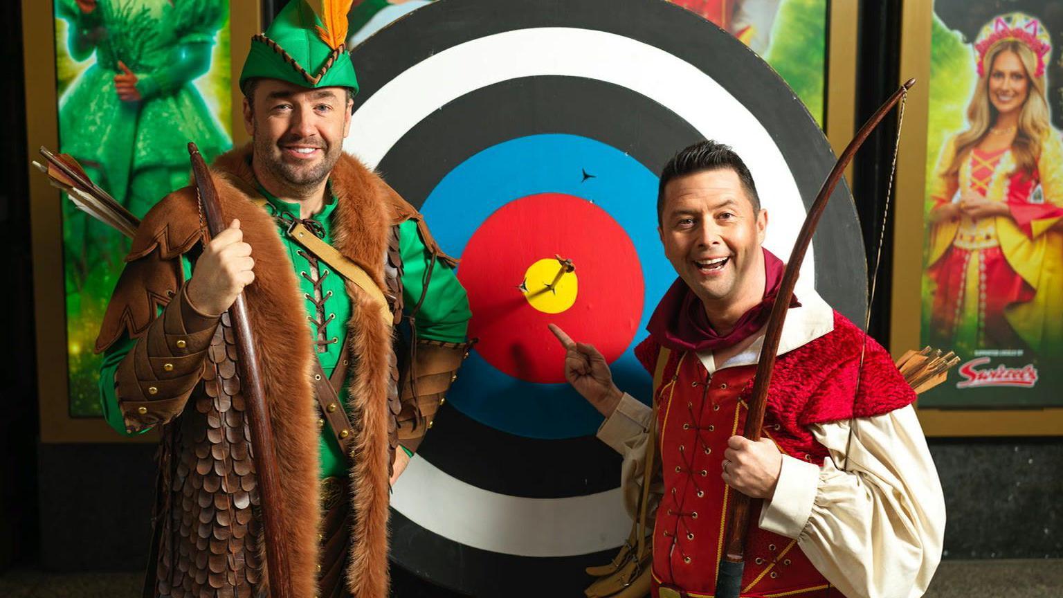 Jason Manford and Ben Nickless in pantomime costume stood in front of a large target