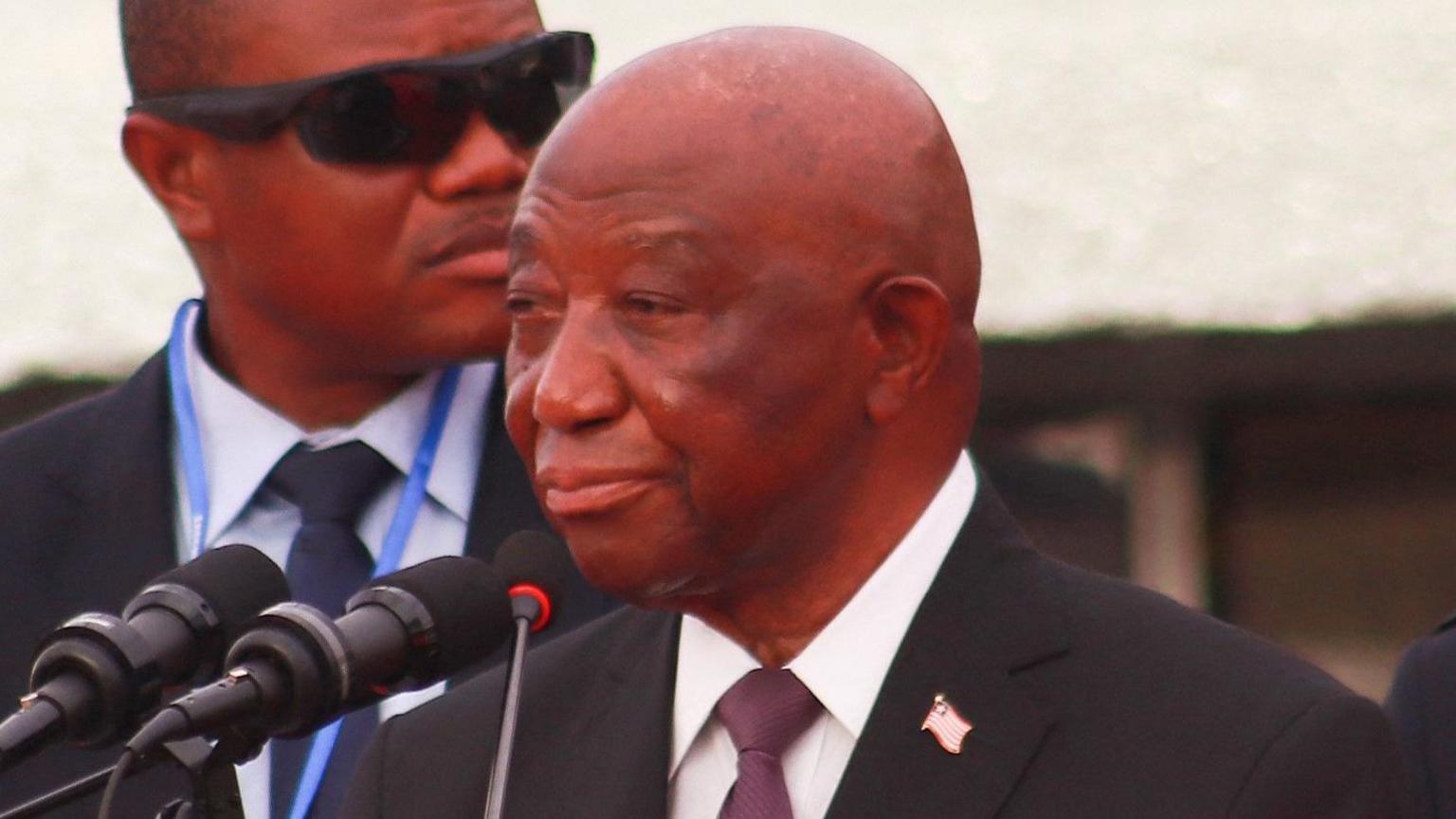 Liberia President Joseph Boakai, in a black suit, white shirt and a tie, speaking to a microphone