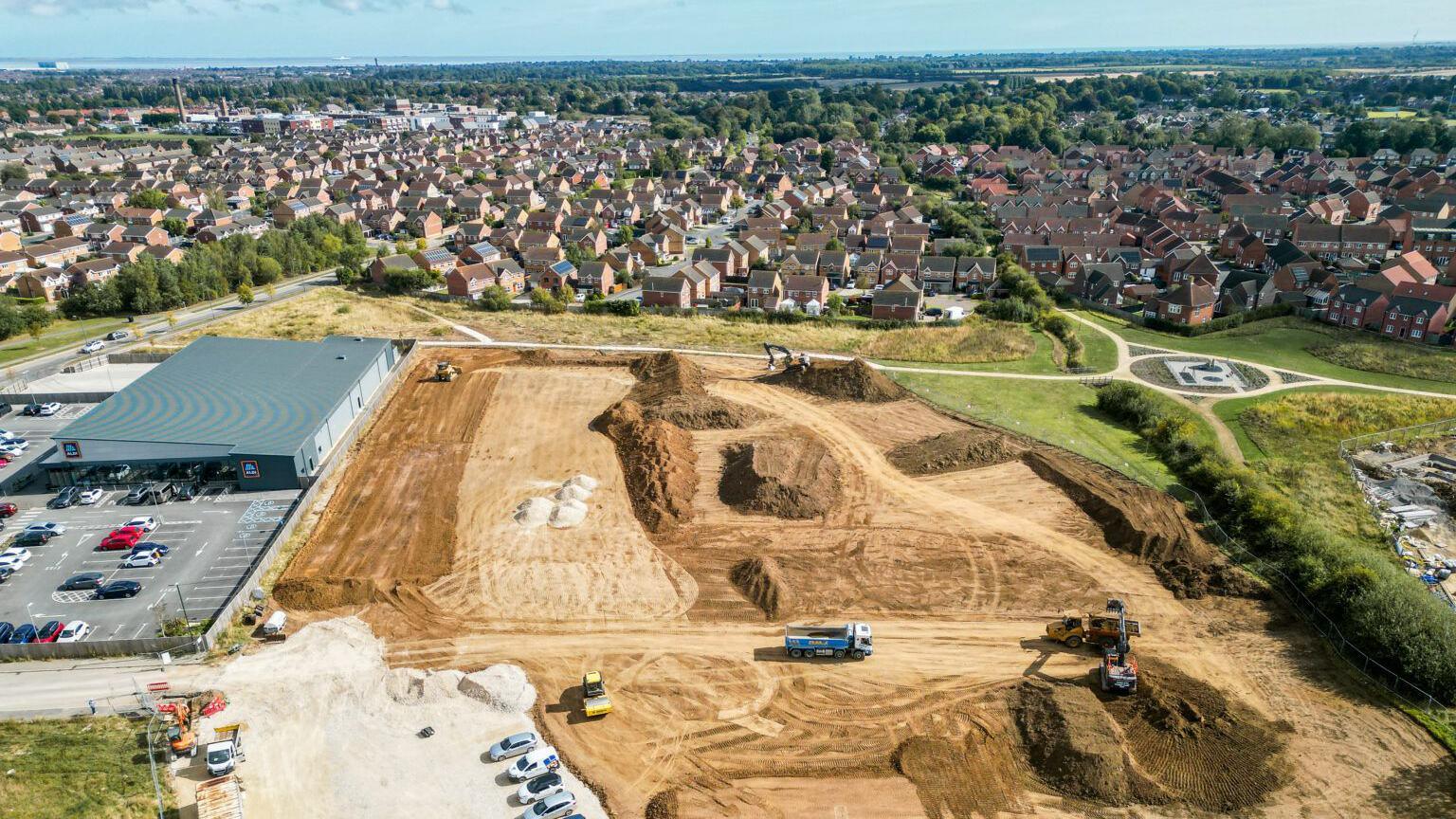 A drone view showing diggers and trucks working on freshly dug ground at the Scartho school site, next to an Aldi store and car park, with rows of houses in the background.