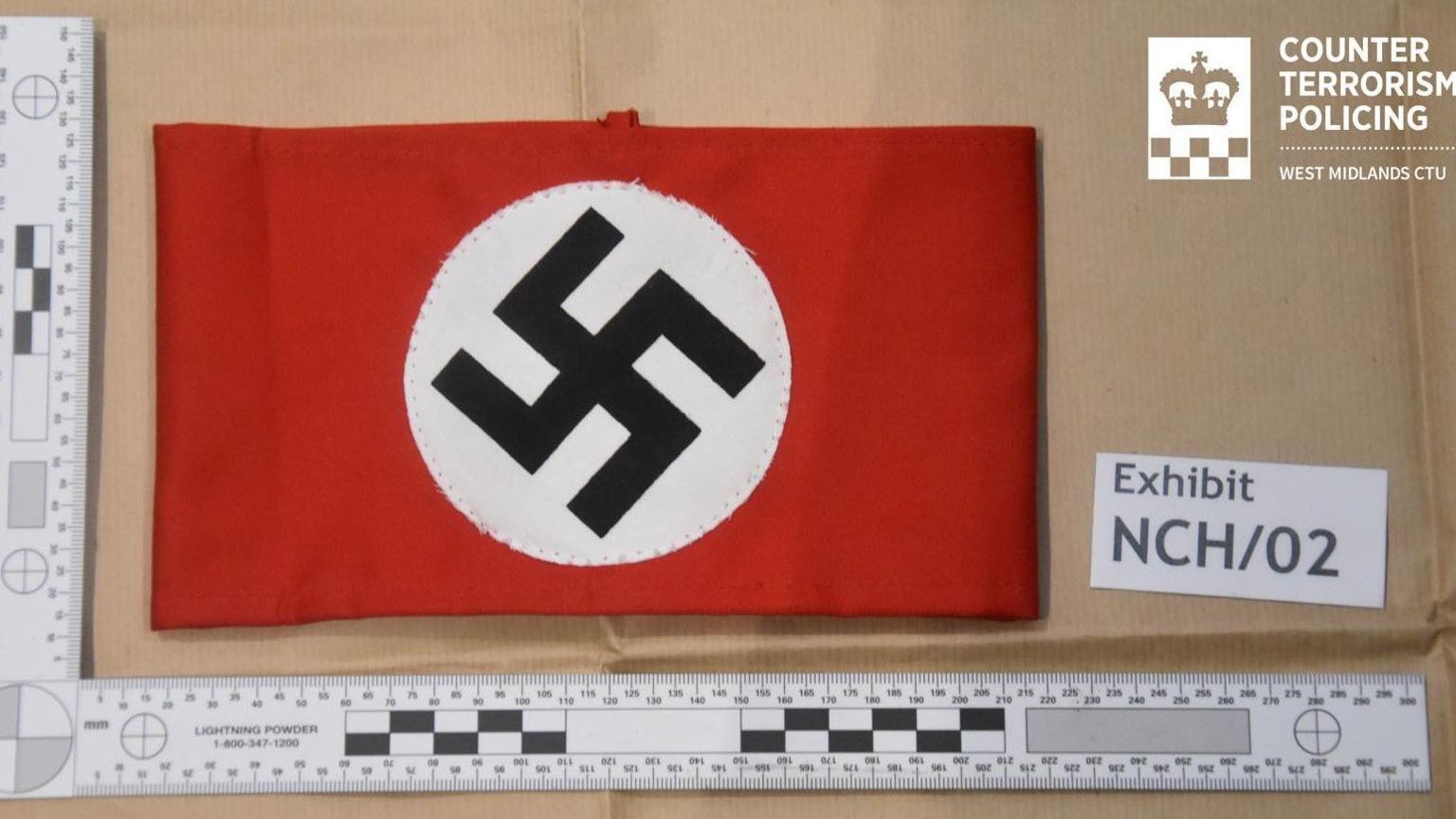 A police image of a piece of red cloth decorated with a Nazi swastika. A label next to it has an exhibit number.