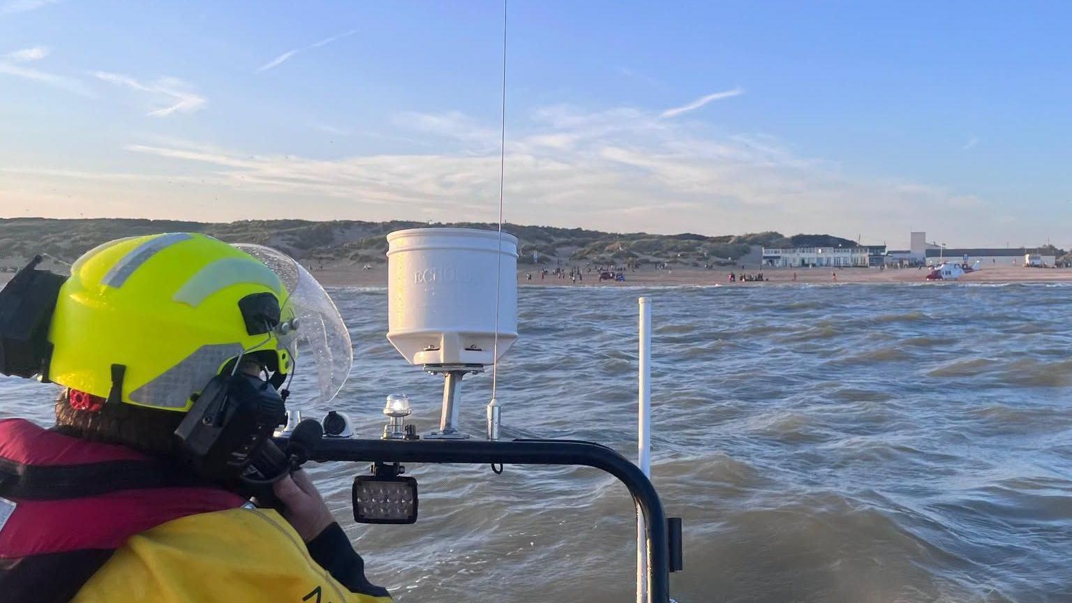 A picture taken from a lifeboat looking back to land, with a man on it making a phone call.