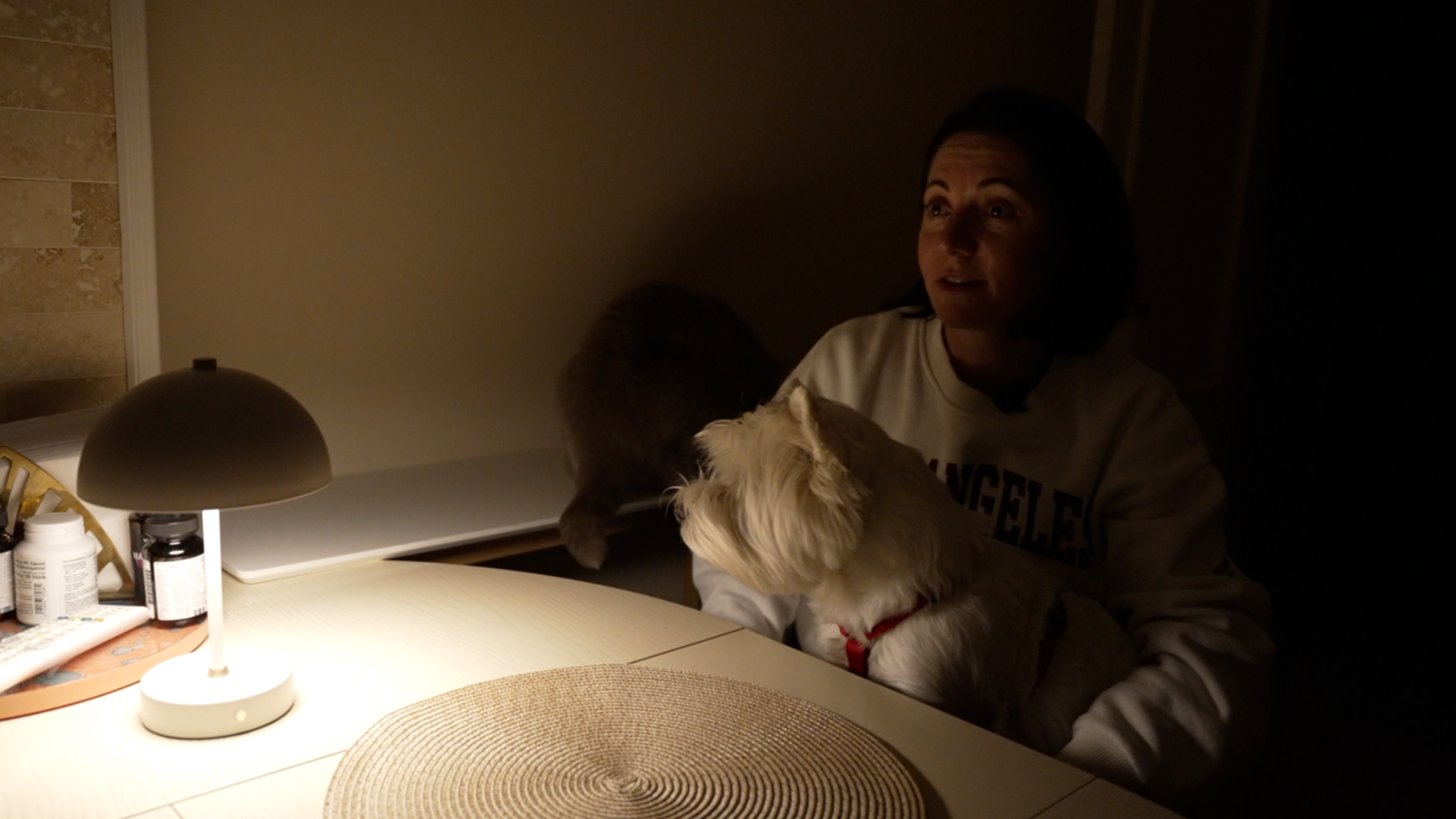 Nataliya sits in a chair in a poorly lit room, with a white dog on her lap