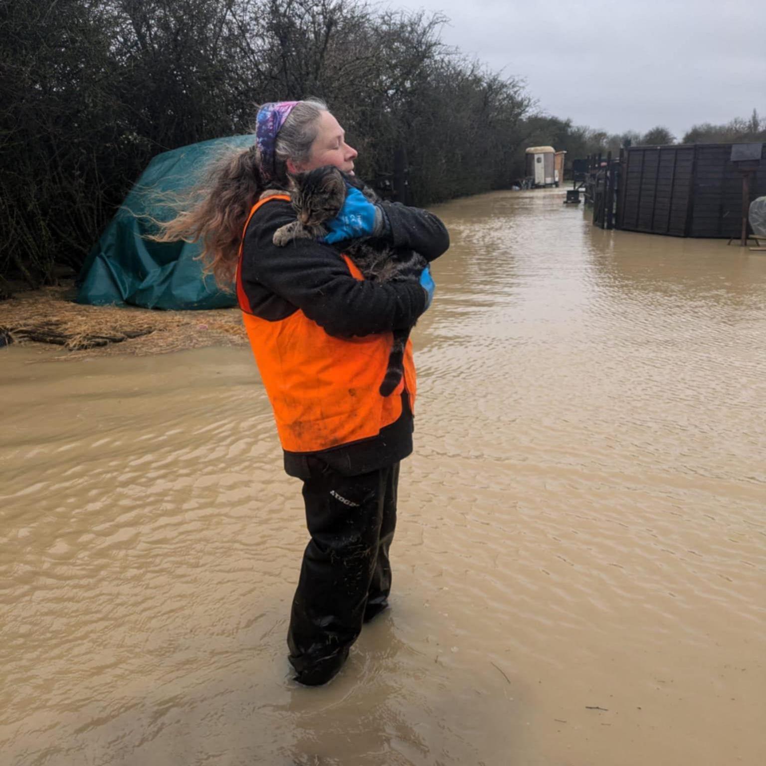 Kathy Owen wearing an orange hig-vis vest standing in flood water and holding a cat