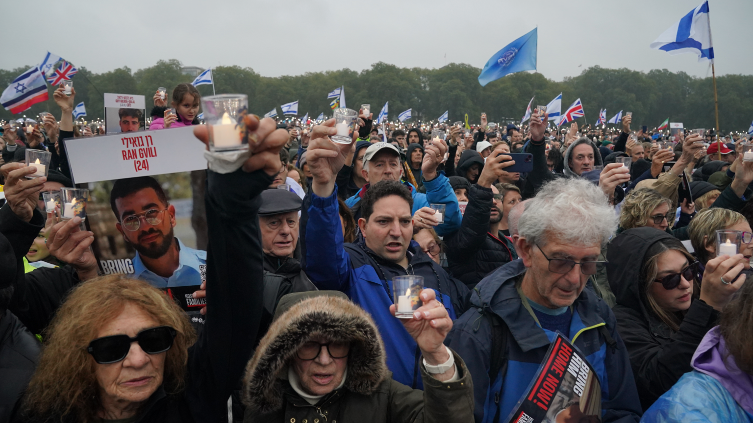 Memorial attendees hold pictures of hostages, candles and wave Israeli flags