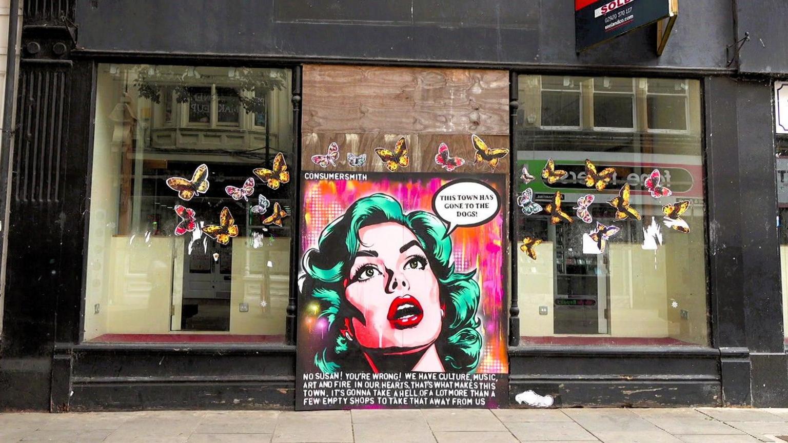 A boarded up shop in Newport with a pop art woman painted onto a board and a speech bubble which reads: "This town has gone to the dogs"