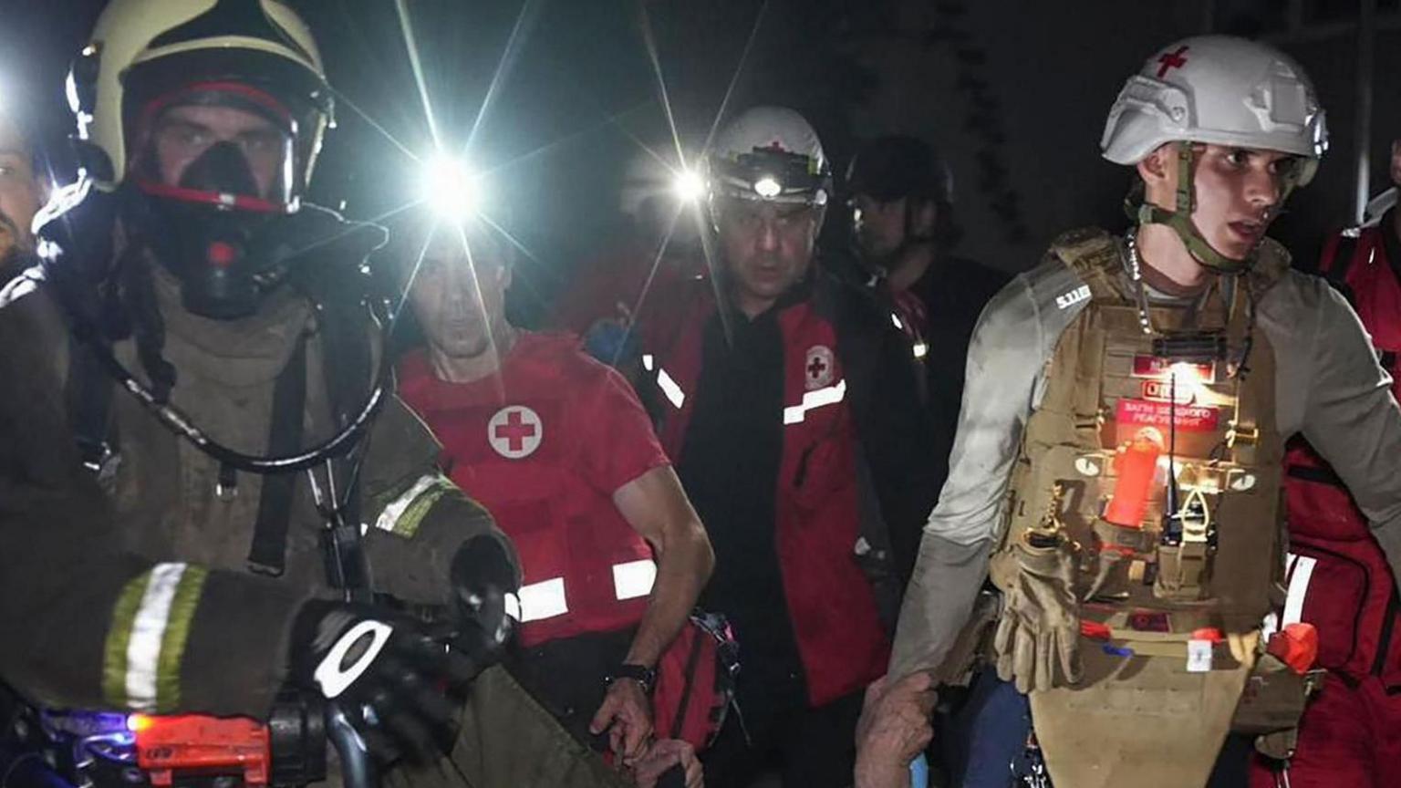 Emergency workers carrying an injured person after a Russian air bombardment.  The four men are in helmets, heavy fire-fighting equipment and flak jackets.