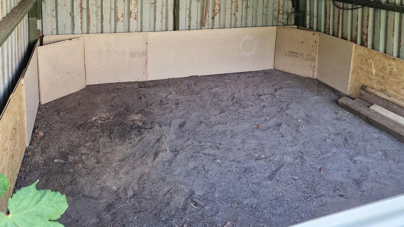 A pit inside a corrugated metal structure, surrounding by wooden panels
