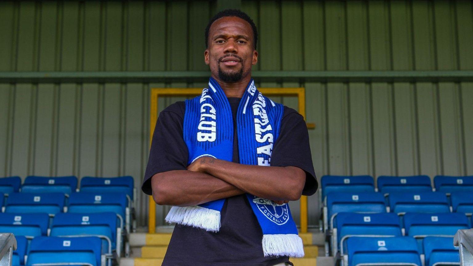 Manny Duku, wearing a blue Eastleigh scarf, poses for a photo at the club's stadium