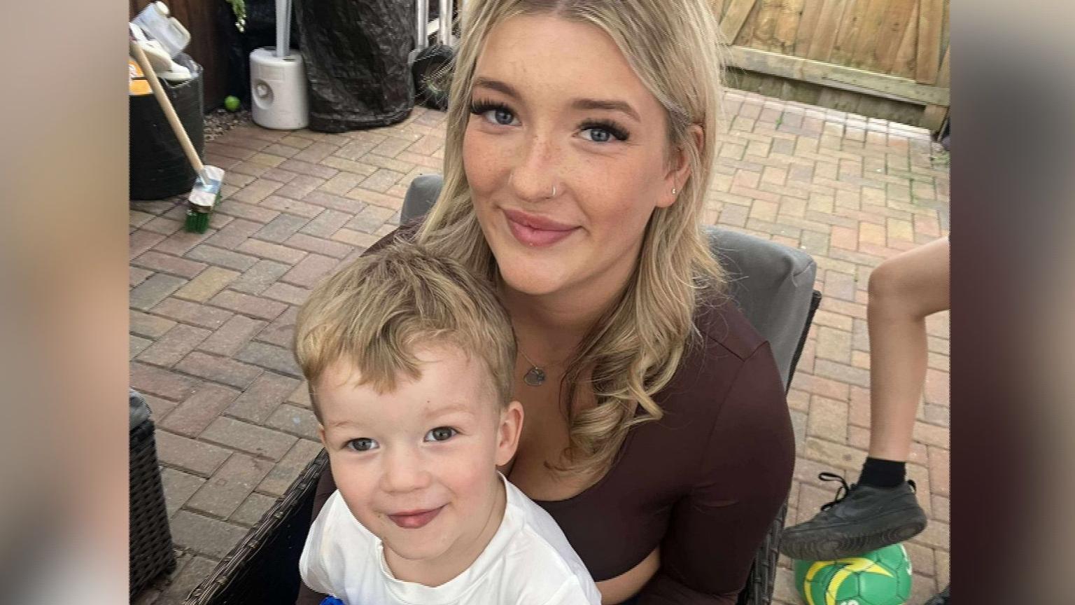 A photo of Chanyta with her three-year-old son Rowan sitting on her lap, both smiling. It is taken by someone who is standing and they are looking up into the camera.