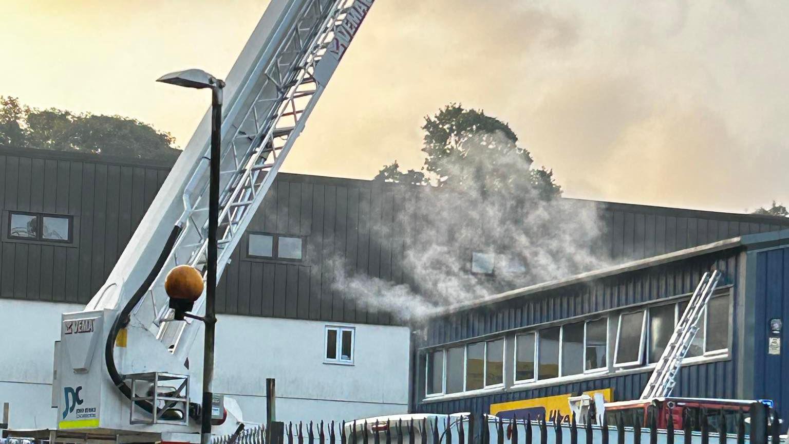 Smoke coming from the top of a blue industrial building in Tavistock with an aerial ladder platform.