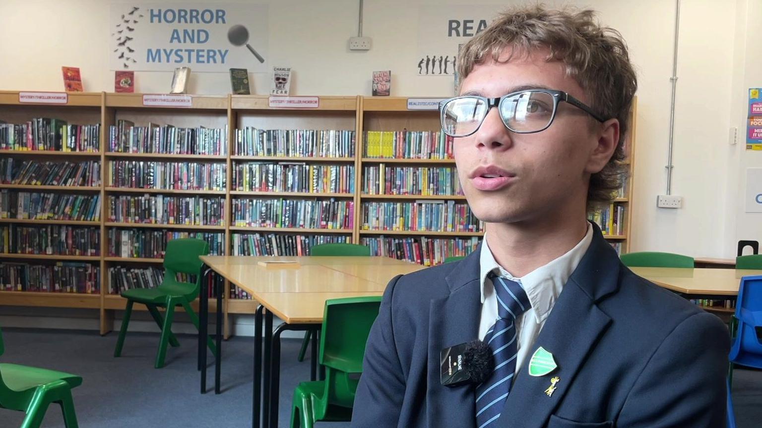 A teenager wearing glasses and a traditional blue school uniform with a white shirt and blue striped tie
