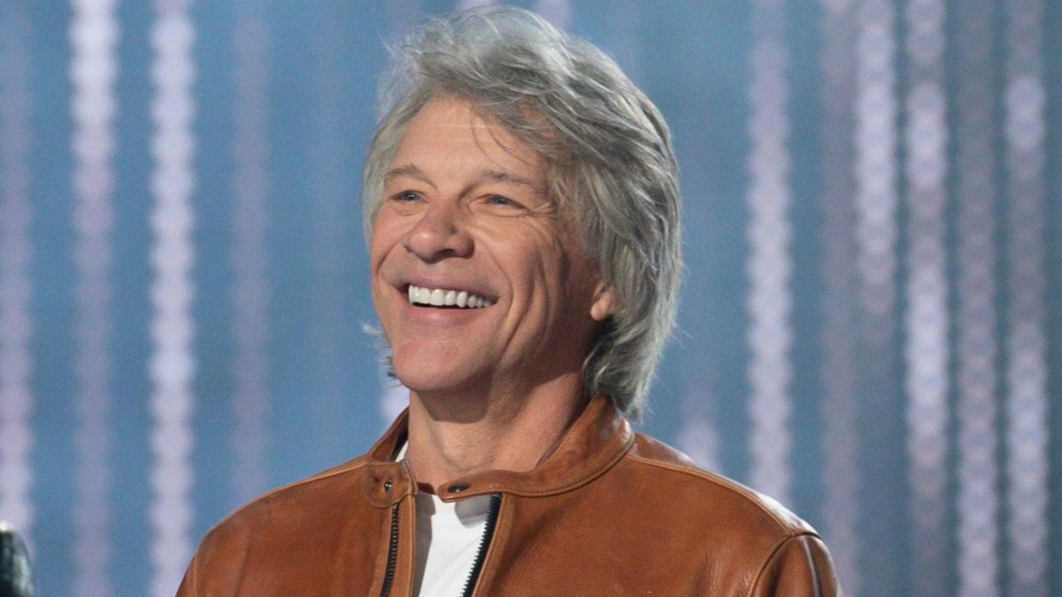 US rock legend Jon Bon Jovi smiles while wearing a white t-shirt and a tan leather jacket while performing on the series America Idol in May 2024.