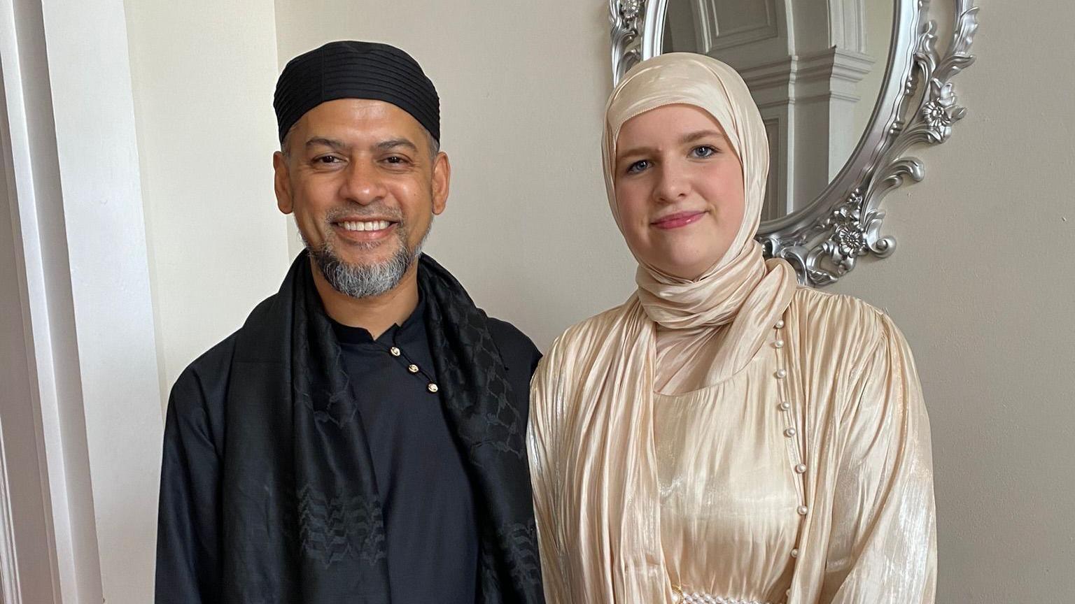 Mohammed Ali wearing all Black as he stands next to his daughter Aleyah, who is wearing a silk hijab and dress.