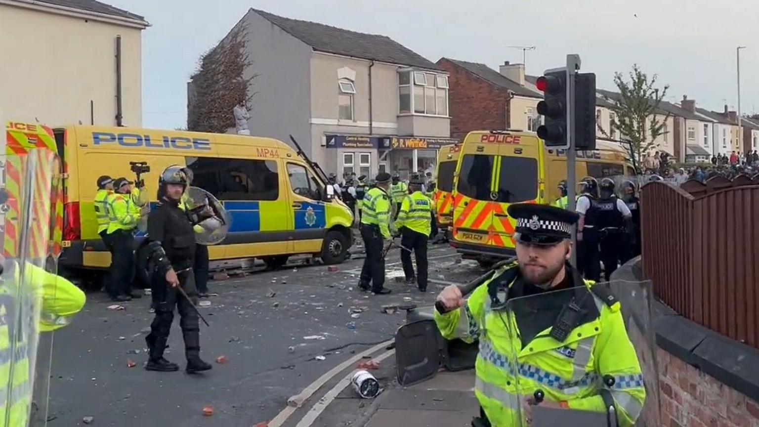 Riot police stand in front of three police vans in Southport during disorder on 30 July