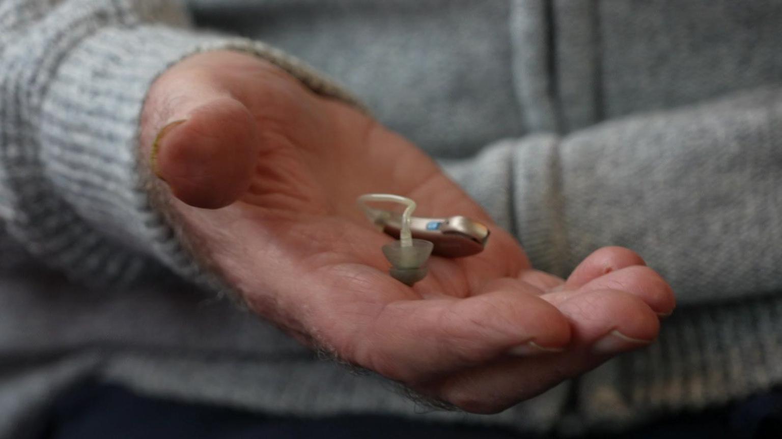 A close-up image of Mr Yarrow's hand. He is holding his hearing aid which is much smaller than his palm. The tube is clearly very small.