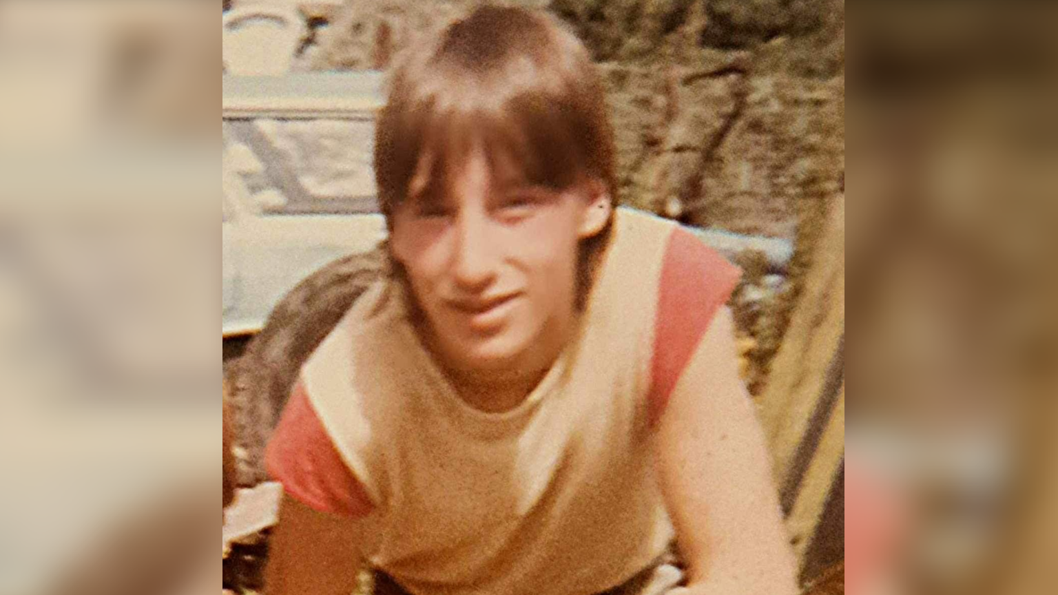 Kevin Roberts looking into the camera and smiling for a photo when he was 12-years-old. He had long brown hair and is wearing a t-shirt.