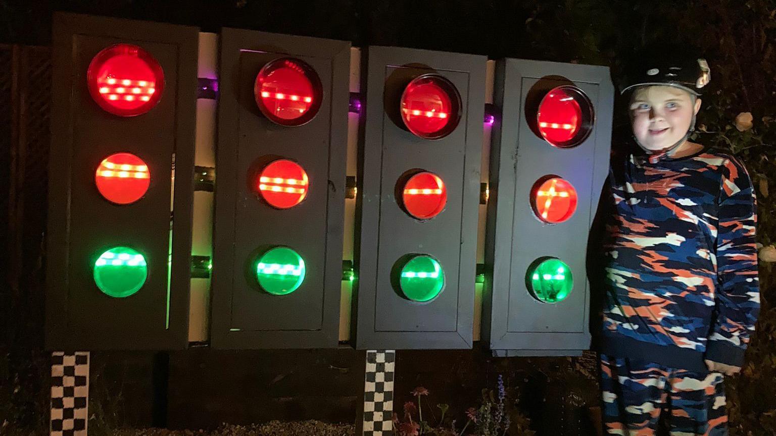 11-year-old Jenson stands in front of new F1-racing lights smiling wearing a helmet.