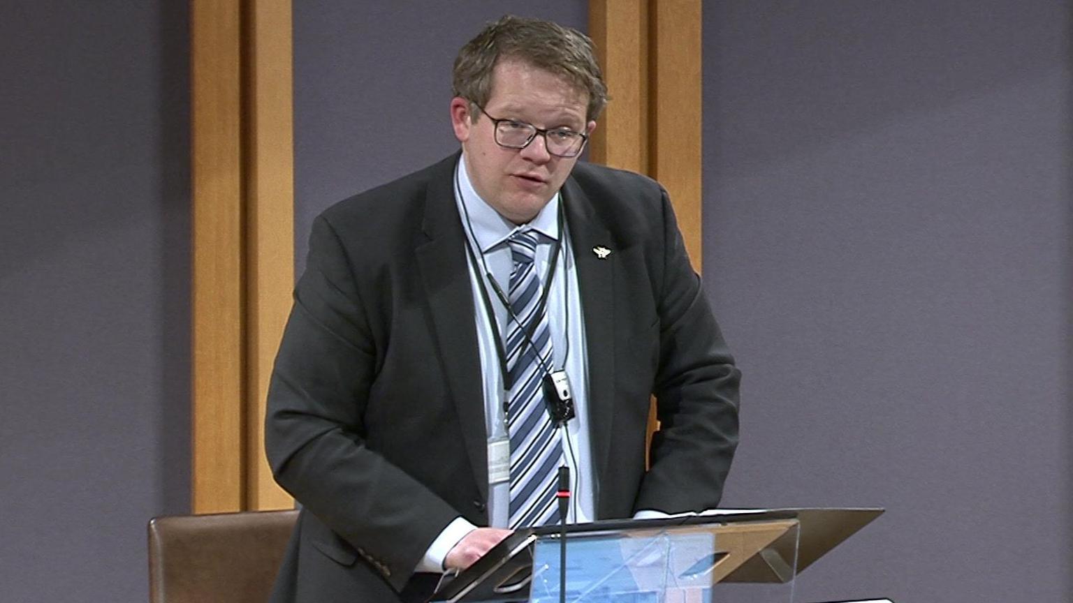 Joel James addressed the Senedd's debating chamber, wearing a black suit, blue shirt and a tie.