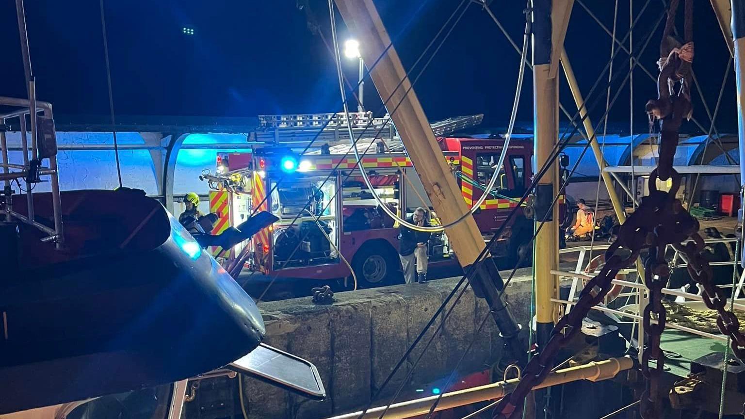 A fire engine at Newlyn Harbour in Cornwall seen through net rigging of the 25m-long vessel which caught fire