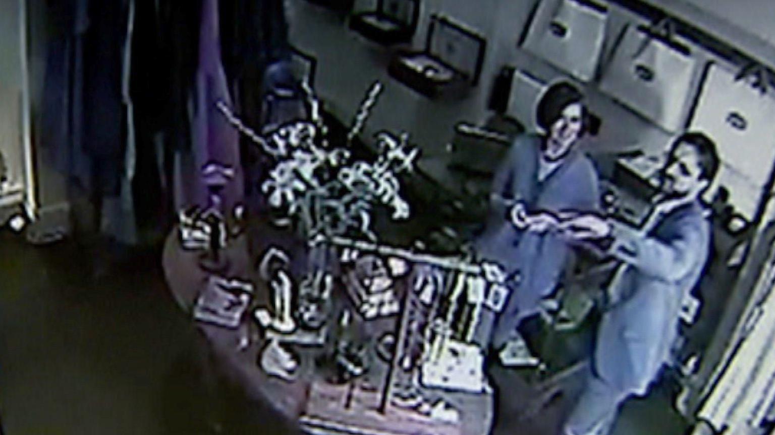 A screenshot of CCTV footage from inside a shop in Tetbury. It shows Mark and Carolyn chatting and smiling in the corner of the room, behind a central display of jewellery and bags. He is wearing a grey suit and she is wearing a grey cardigan, with her dark hair cut into a short bob.