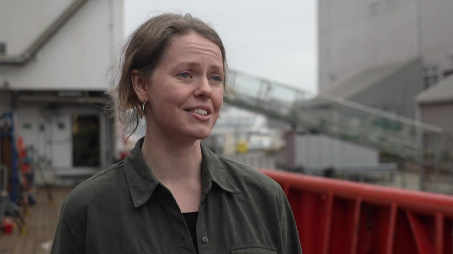 Dr Rhiannon Jones looking to the right and smiling. She is wearing a dark green shirt and is stood on the ship.