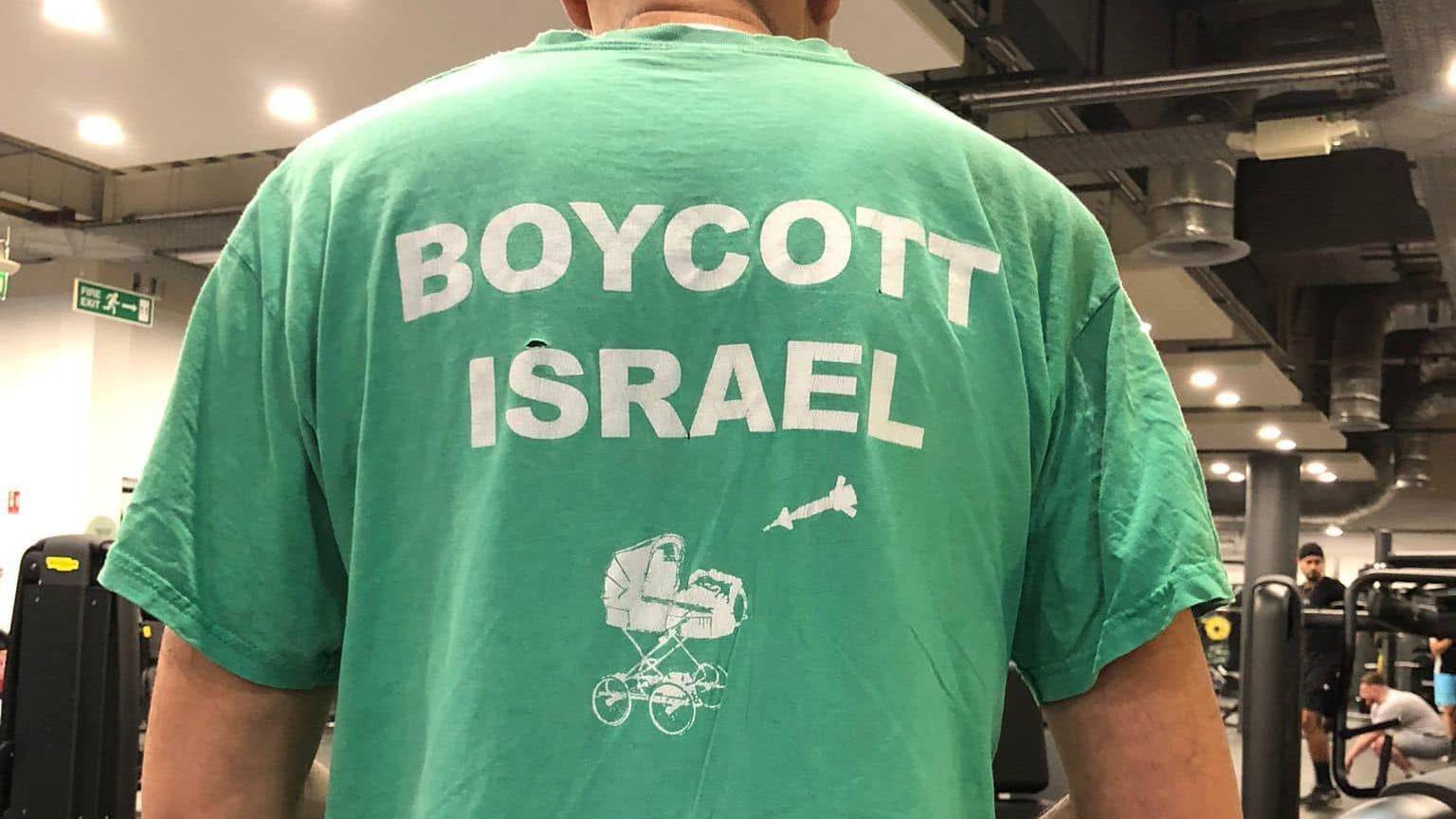 A man with his back to the camera wearing a green t-shirt with the words 'Boycott Israel' written on them and a picture of a pram and a missile