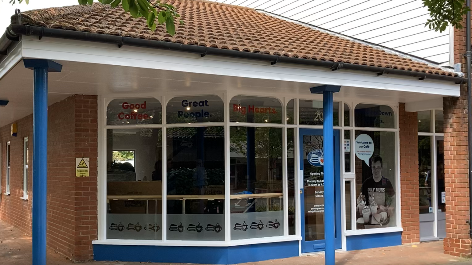 The outside of the new cafe. It has large windows on its front that surround the entrance. Two blue pillars stand in front of the entrance. 