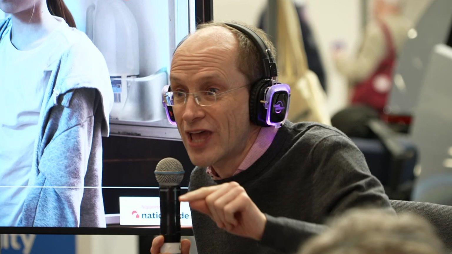 Tim Leunig, a bald middle-aged man with spectacles, holds a microphone and uses his finger to make a point during an impassioned speech at a Labour fringe meeting
