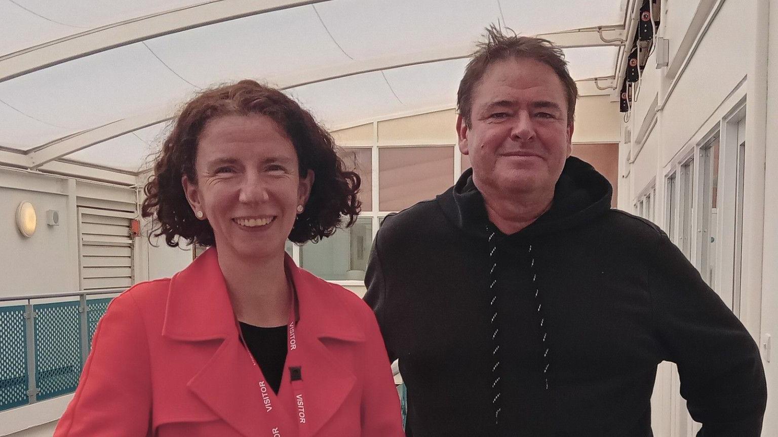 Anneliese Dodds wearing a pink blazer and pink visitor lanyard smiles into the camera next Toby Blake, who is wearing a black hoodie and also smiling 