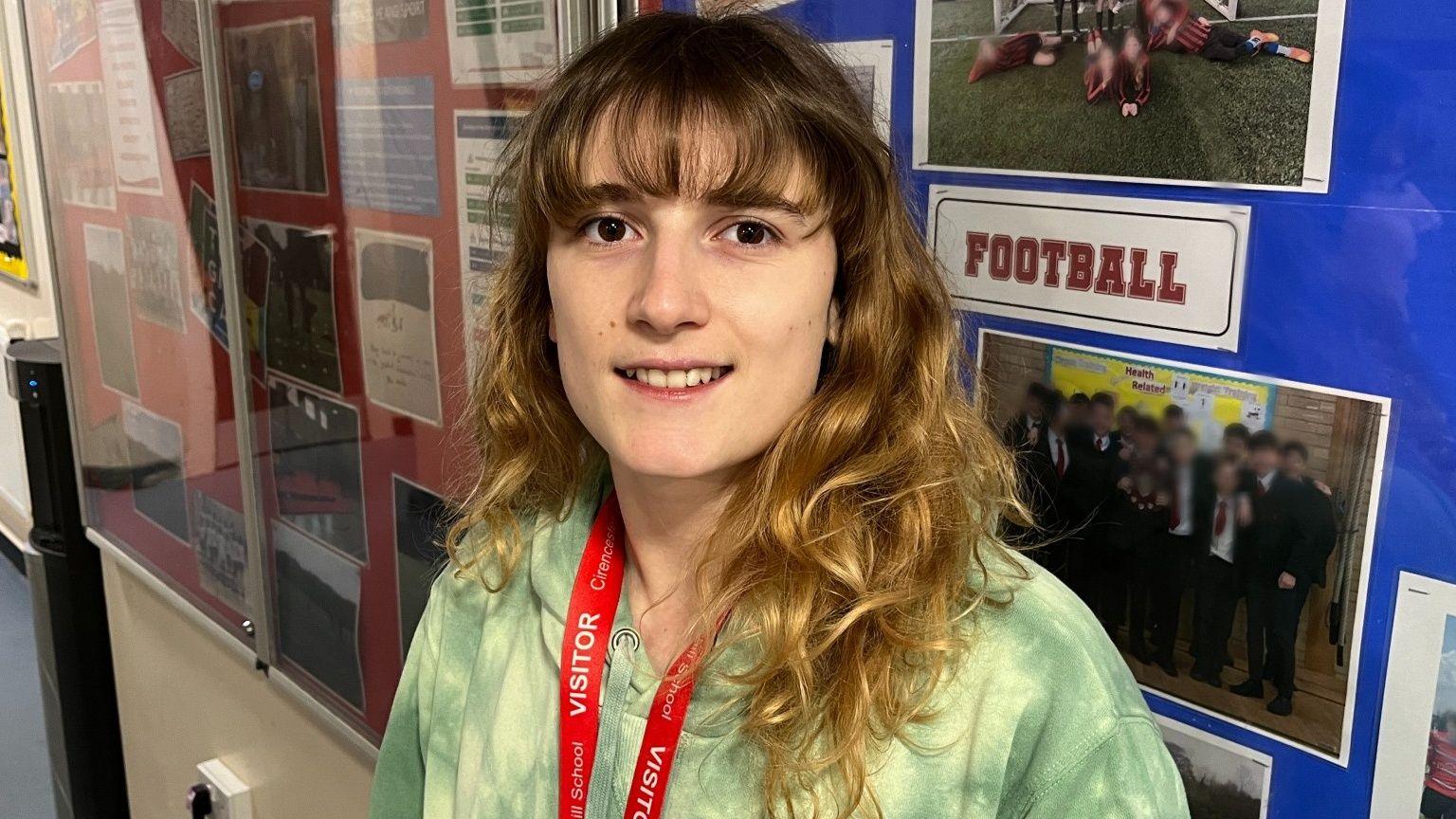 Anya Hutin - Project Coordinator for the IOPC Youth Panel smiling in front of a sports board in the PE Department of Cirencester Kingshill Secondary School