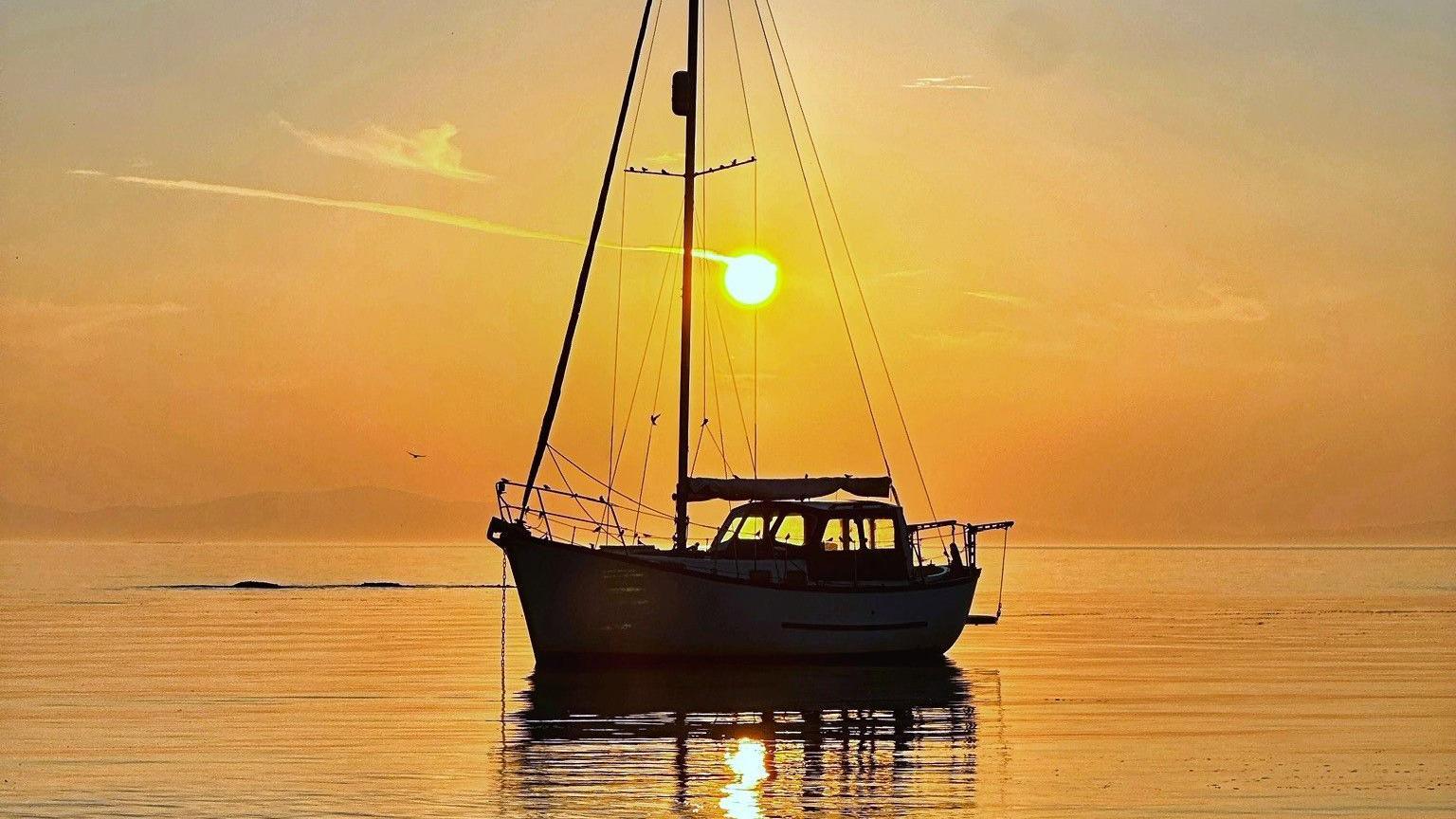 A boat silhouetted by the sun. The light has turned the sky and water a deep orange.