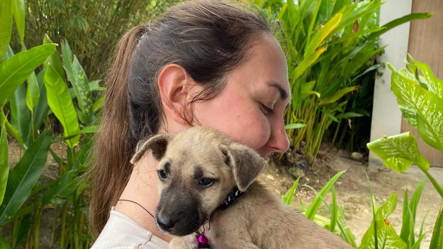 A woman with long dark hair hugs a small brown puppy