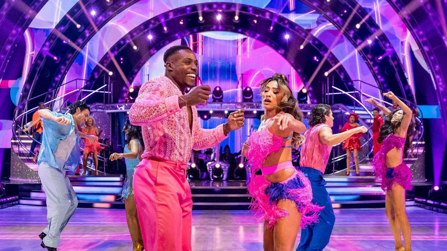 Harry Aikines-Aryeetey - aka Nitro from Gladiators - with Karen Hauer, his dance partner, performing in bright costumes on the Strictly floor.