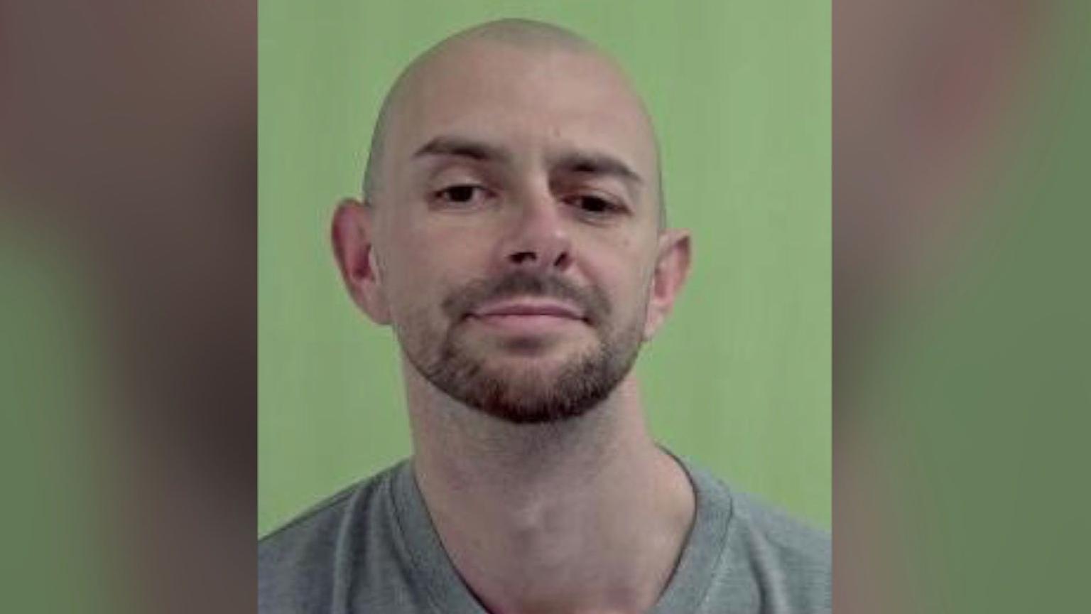 A mugshot of Jamie Skillen a bald man with brown stubble with a green background.