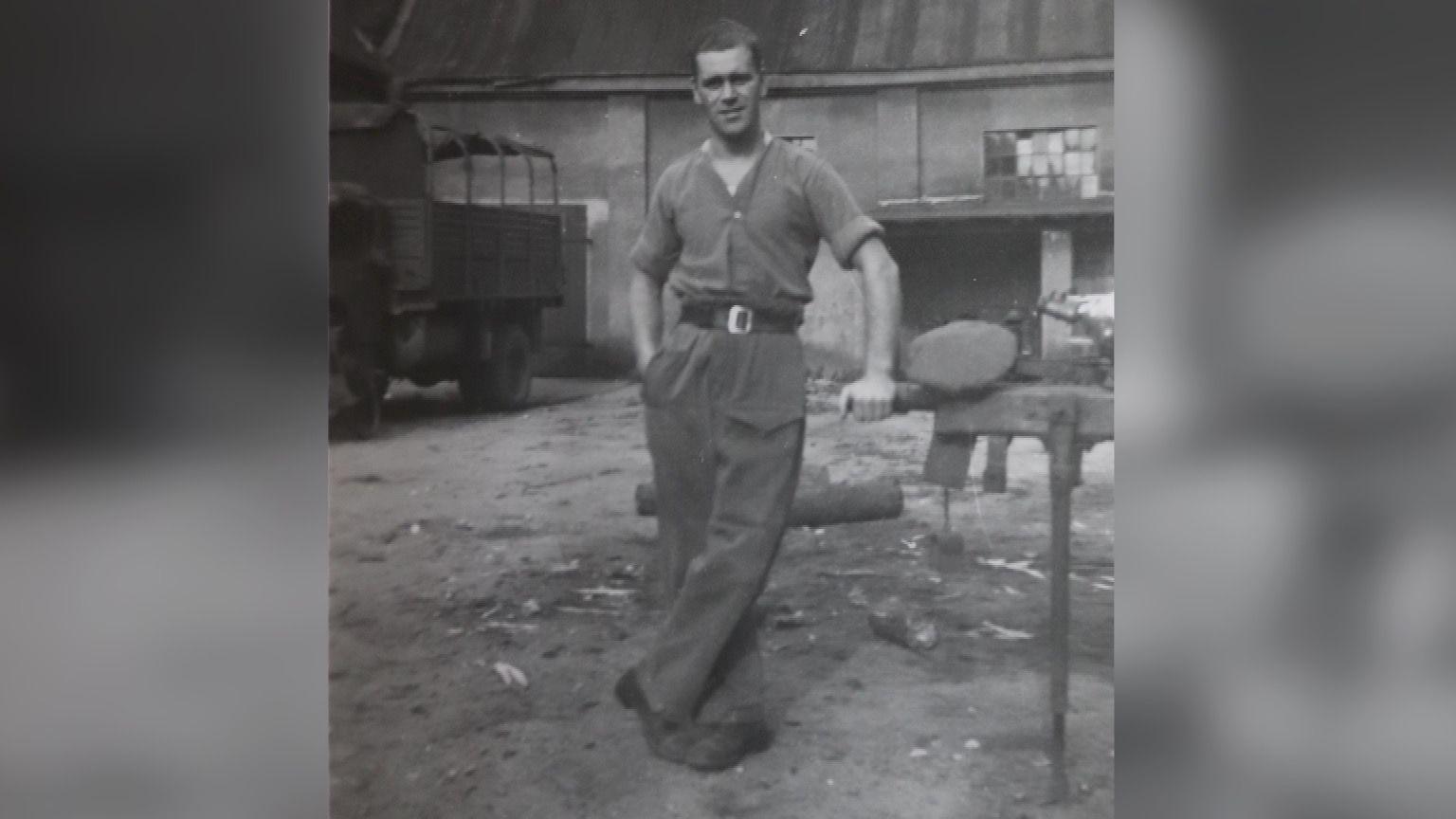 A black and white photo of Monty, taken in an unidentified location while serving in Europe. He is a young man in the photograph with short brown hair. He is in his shirt sleeves and in high waisted military trousers.